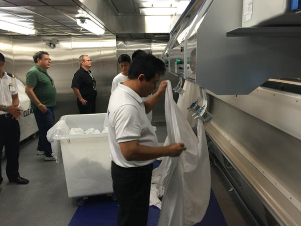 One of the laundry workes on Quantum of the Seas loads a sheet into a giant presser