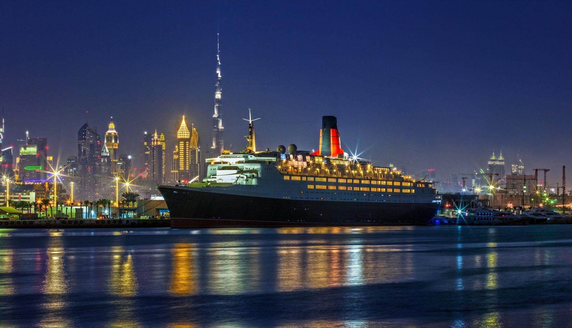 The QE2 docked in Dubai at night. Photo credit: PCFC Hotels